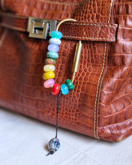 Bag charm artesanal con piedras naturales ópalo, jade y cuarzo colgando en una cartera.